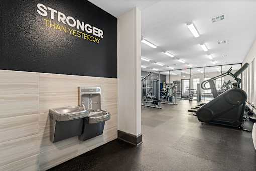 A gym with a wall that says "STRONGER THAN YESTERDAY" and a treadmill in the background.
