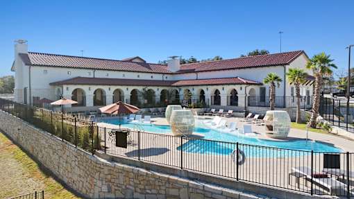 A large white building with a red roof and a pool in front.