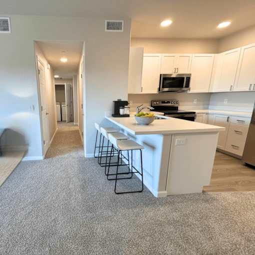 A kitchen with white cabinets and a white island with a bowl of fruit on it.