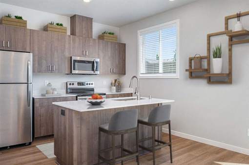 A kitchen with a refrigerator, microwave, oven, sink, and two chairs.