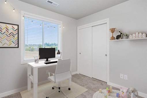 A white desk with a computer monitor and chair in a room with a window.