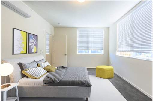 A bedroom with a bed, a yellow stool, and two framed pictures on the wall.