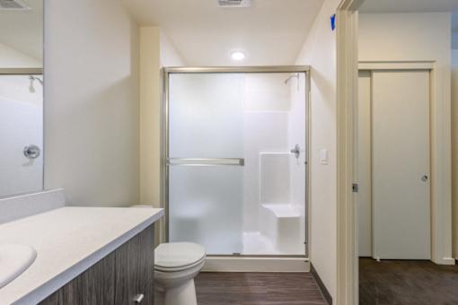 A white bathroom with a toilet, sink, and walk-in shower.
