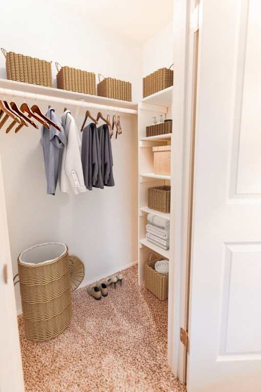 A white closet with clothes hanging and shelves with baskets.