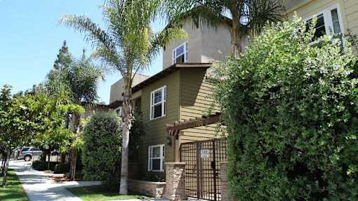 A house with a brown fence and a gate is surrounded by green trees.