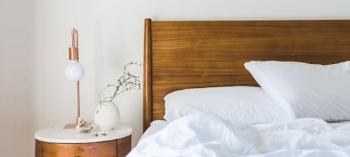 A bed with white pillows and a white bedspread is next to a wooden headboard.