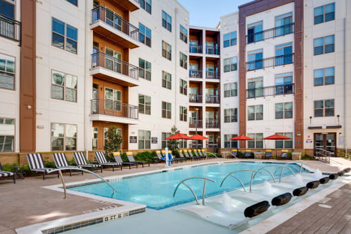 a swimming pool with chaise lounge chairs and umbrellas in front of an apartment building