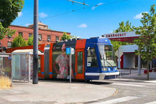 A blue and orange tram is parked in front of a building with an emergency sign on it.