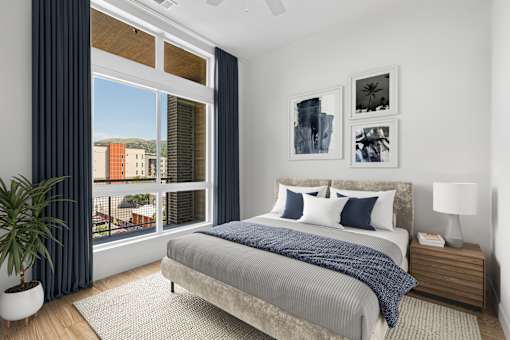 A bedroom with a large bed and a view of a cityscape through the window.
