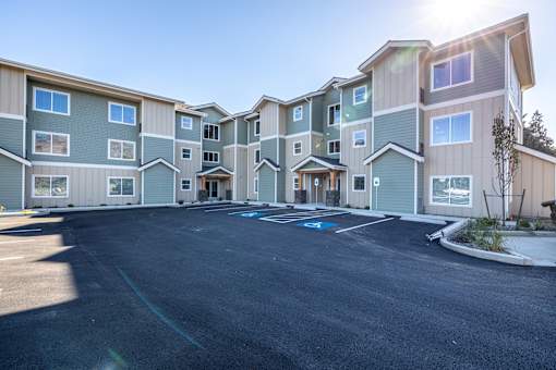 A sunny day at a large apartment complex with a parking lot in front.