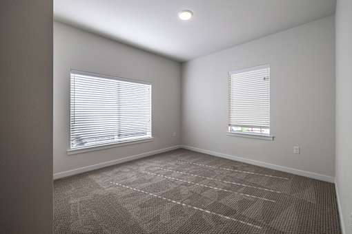 A room with carpeted floor and two windows with blinds.