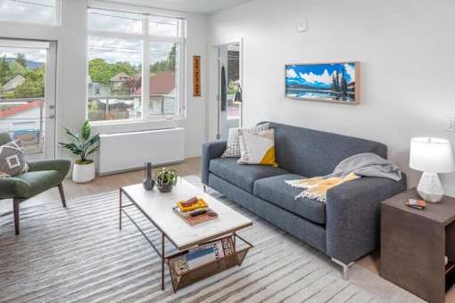 A living room with a grey couch, a green chair, a white coffee table, and a painting on the wall.
