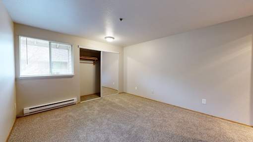 A carpeted bedroom with a large window at Heron Hills apartments in Gresham Oregon.
