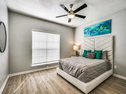 A bedroom with a bed, a ceiling fan, and a painting on the wall.