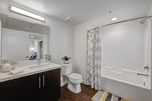 Pet Friendly Apartments in Hollywood CA - The Fifty Five Fifty - A Spacious Bathroom With White Countertops, Dark Cabinetry, Wood-Style Flooring, And A Full Shower/Tub Combo