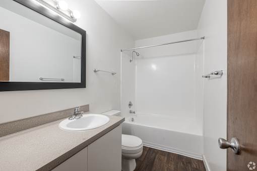 Bathroom with tub/shower combo, white walls, and dark, wood-style flooring at The Groove apartments in the Hazel Dell 98665 neighborhood in Vancouver, Washington.