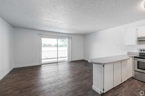 Spacious kitchen with open floorplan island looking out into living room space with dark, wood-style flooring at The Groove apartments in the Hazel Dell 98665 neighborhood in Vancouver, Washington.