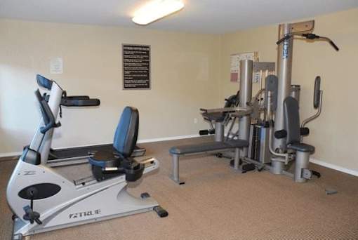 A gym room with a rowing machine, a bench, and a weight machine.