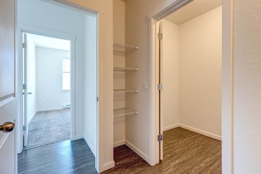 A hallway with a door on the left and a closet with shelves on the right.