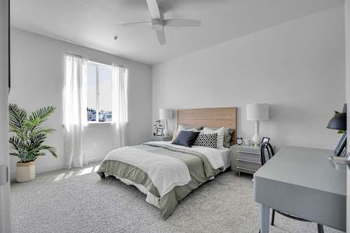 A bedroom with a bed, nightstand, and a plant.