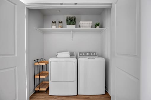 A small laundry room with two washing machines and a shelf above them.