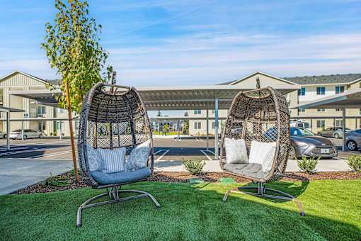Two hanging chairs are placed on a lawn in front of a building.