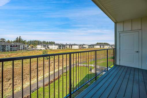 A balcony with a black railing overlooks a grassy area and a road.