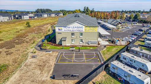 A Now Leasing office is located in a parking lot with a basketball court.