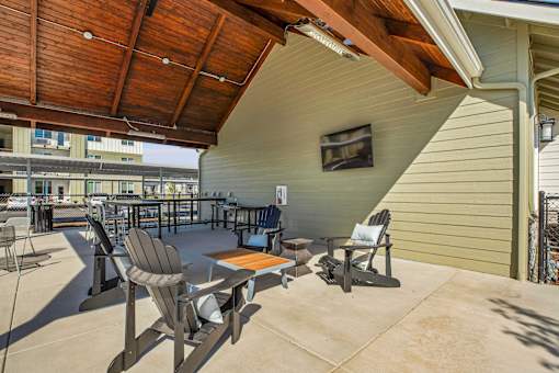 A patio with a table and chairs under a wooden roof.