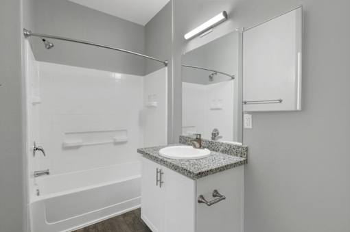 A white bathroom with a sink, mirror, and bathtub.