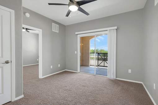A room with a ceiling fan and sliding glass doors leading to a balcony.