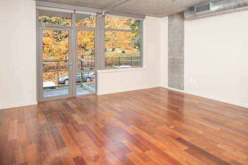 A room with a wood floor and a view of trees outside through a glass door.
