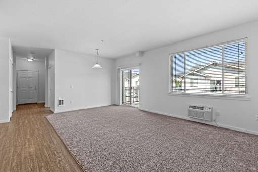 A large, empty room with a carpeted floor and a window with blinds.