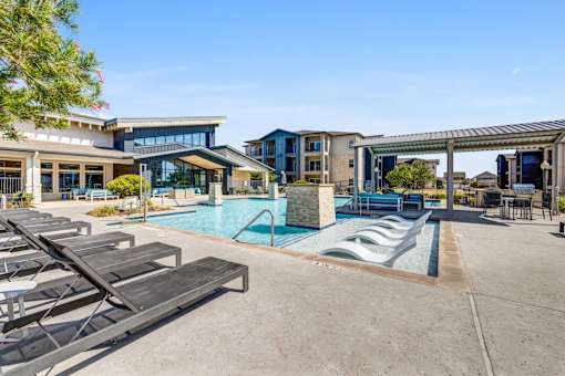 A pool area with sun loungers and a building in the background.