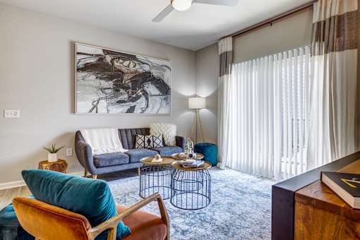 A living room with a blue couch, a chair, a table, and a painting on the wall.