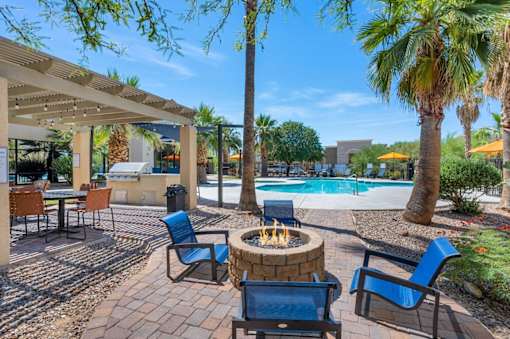 A patio with a fire pit and chairs.