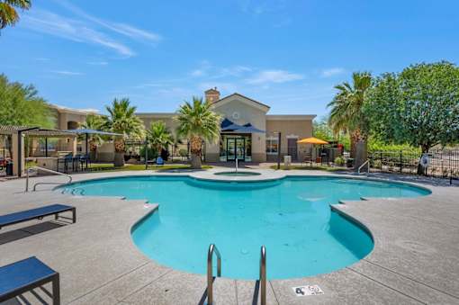 A large swimming pool surrounded by a concrete patio and a small building in the background.