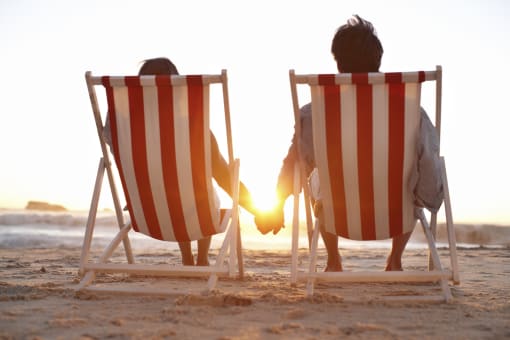 two people sitting in deck chairs on the beach at sunset