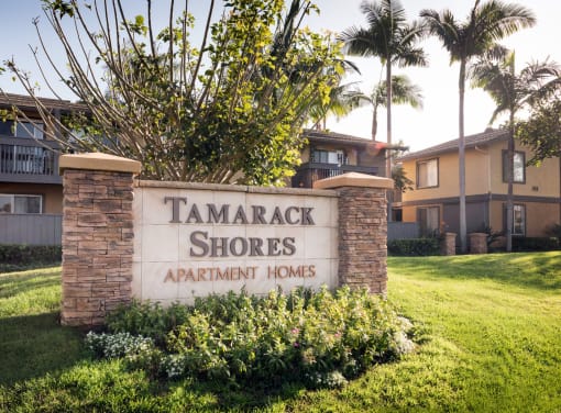 a sign for tamarack shores apartment homes in front of a lawn and trees