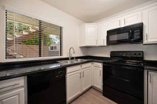 a kitchen with black appliances and white cabinets and a window