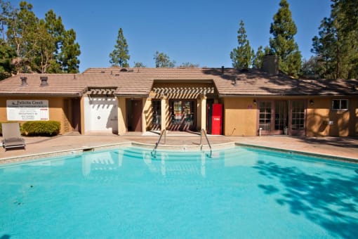 a swimming pool in front of a brown building with a red door