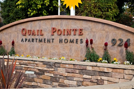 a stone wall with a sign for quail point apartments homes
