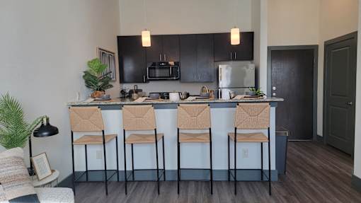 A kitchen with black cabinets and a bar area with four chairs at Urban Square, Denton, TexasX, 76210