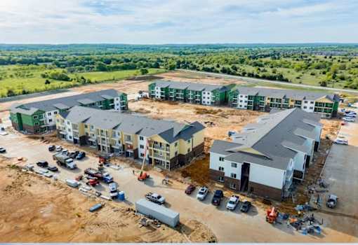 A construction site with partially completed buildings and a parking lot with several cars.