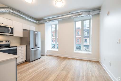 an empty living room with a kitchen with stainless steel appliances and a large window