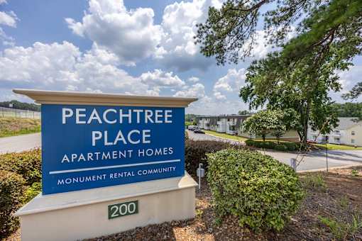 A sign for Peachtree Place Apartment Homes in front of a tree.