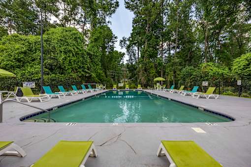 A large outdoor swimming pool surrounded by trees and lounge chairs.