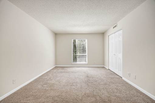 A room with a carpeted floor and a window with blinds.