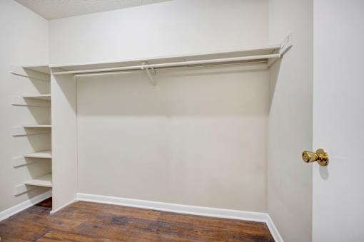 A white closet with a wooden floor and a gold door handle.
