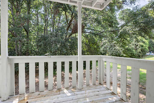 A white wooden porch with a roof and railings overlooking a wooded area.